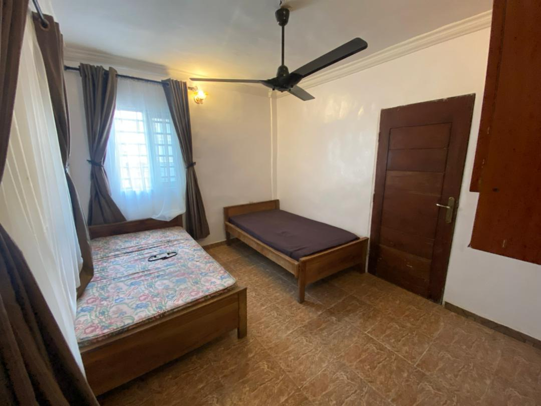 Spacious bed space room with ceiling fan, curtains and two separate wooden beds at Rilwan AJALA Homes